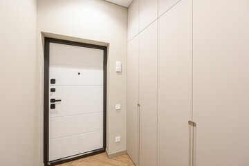 modern entryway with a white door framed in dark trim, next to a beige wardrobe. Clean lines and neutral colors create a minimalist aesthetic