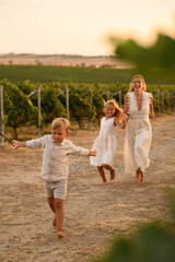 Happy mother with little son and daughter running, laughing and spinning together in sunny vineyard, enjoying carefree childhood and family time outdoors.