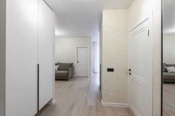 Bright, modern hallway with white doors and a wardrobe. A glimpse of a living room with a sofa is visible