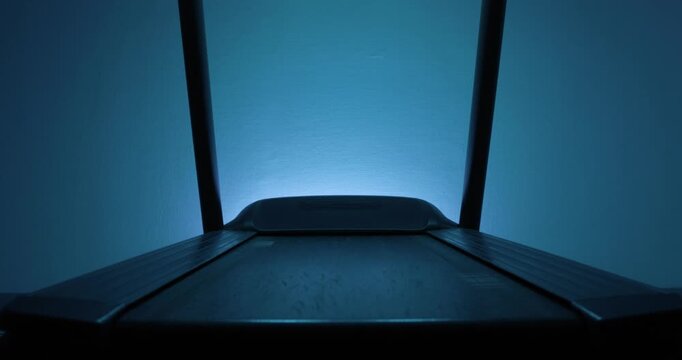 Close-up of an empty treadmill in a futuristic blue ambient light.