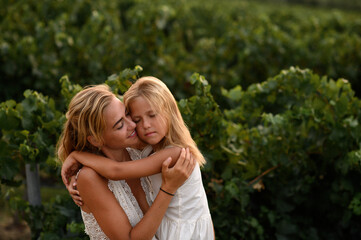 Fototapeta premium Mother hugging her little daughter outdoors, showing love, tenderness and emotional family bond in a natural summer setting.