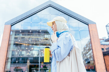 Fototapeta premium Turkish woman in hijab drinking coffee outside modern building
