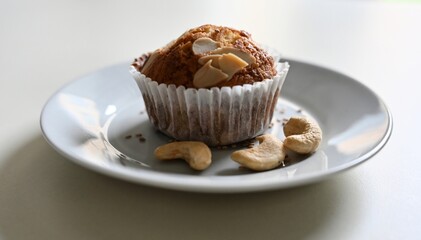 Freshly baked homemade muffin with nuts on a plate, surrounded by cashews and seeds. A cozy, close-up shot capturing the warmth, texture, and love of artisanal home baking.