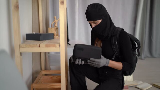 Female thief in black balaclava action housebreak. Robber criminal entering a house for stealing Housebreak in daytime