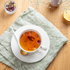 A cup of herbal tea with lemon and bouquet of flowers on a wooden table with napkin.