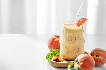 Smoothie with peach and banana in a glass on a wooden board on a white table near window
