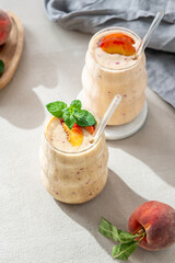 Two glasses of smoothie with peach and banana in a glass on a light background with tropical fruits