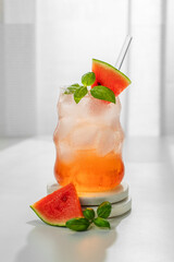 Watermelon mojito cocktail with ice and mint in a glass on a marble stand on a white table near window