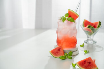 Watermelon mojito cocktail with ice and mint in a glass on a white table near window with fresh slices