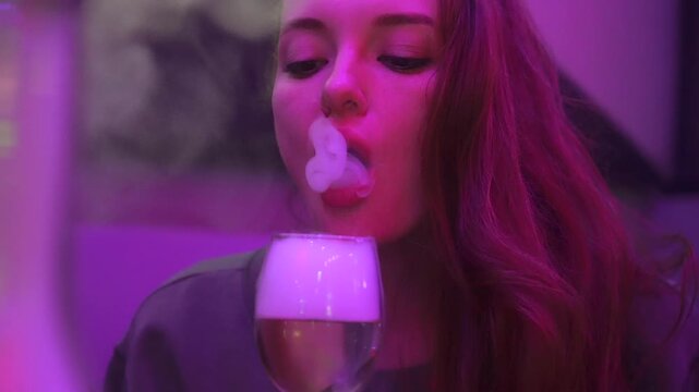 A woman enjoying hookah and exhaling smoke in vibrant neon lighting, creating a modern, stylish, and atmospheric lounge setting.