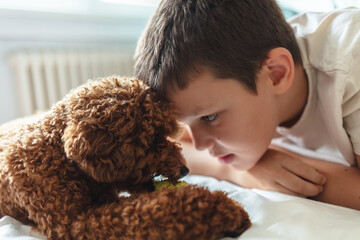 Shot of an adorable little boy playing with his pet dog on the bed at home. Little child, boy, lying in bed with pet dog, little apricot toy puddle.