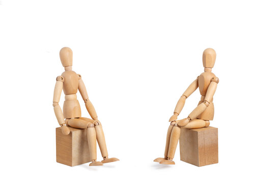 Two wooden mannequins sitting on wooden blocks isolated on a white background