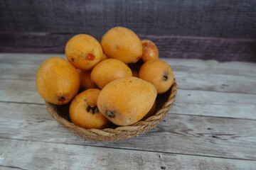 Fresh loquats resting in a woven basket on rustic wooden table