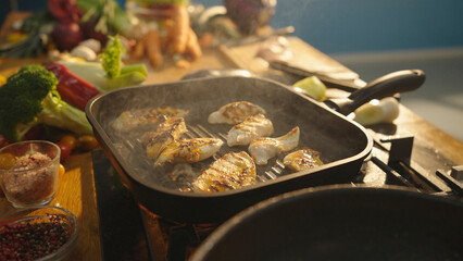 Chef grilling chicken breast fillets in a pan with fresh vegetables nearby