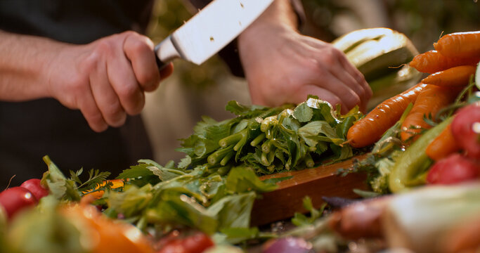 Chef cutting celery on wooden board with fresh vegetables