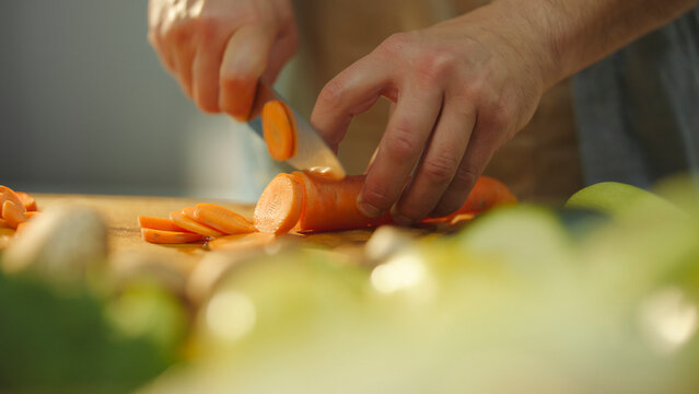 Chef slicing fresh carrots on wooden cutting board - Powered by Adobe