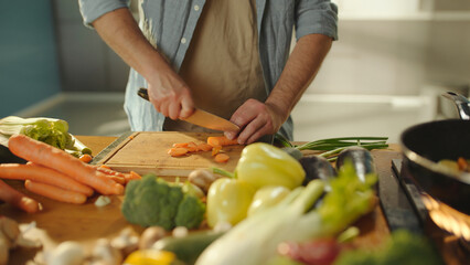 Chef chopping carrots on wooden cutting board surrounded by fresh vegetables