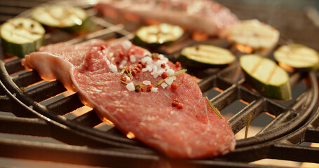 Juicy steak grilling with salt, pepper and rosemary alongside zucchini slices