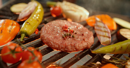Juicy burger grilling with vegetables and spices on barbecue grill
