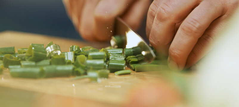 Chef cutting spring onions on wooden board in kitchen