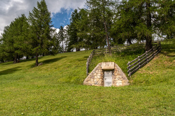 Kleiner Steinkeller zur Wasserquelle mit Metallt&uuml;r auf Almwiese in S&uuml;dtirol