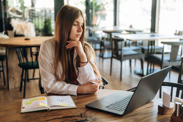 Student is with laptop. Young woman is in the cafe at daytime