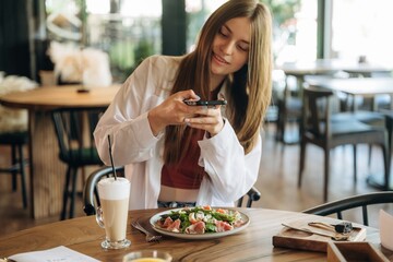 Taking a photo of food. Young woman is in the cafe at daytime