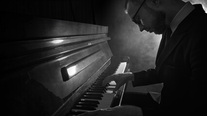 Man in suit playing piano in dramatic monochrome lighting with deep focus and emotion. Concept of jazz performance, music promotion, concert posters, cultural events, and art projects.