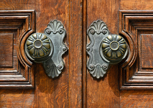 Pair of large ornate metal door knobs on old wooden door