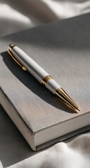 A white pen with gold accents rests on a muted gray notebook. Soft light casts gentle shadows