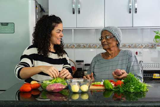 Candid Moment of Latina Woman Cooking with Elderly Afro Grandmother at Home