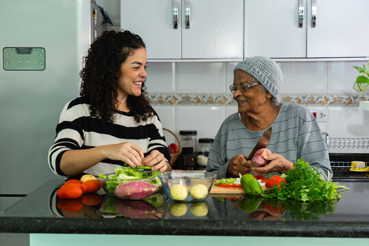 Candid Moment of Latina Woman Cooking with Elderly Afro Grandmother at Home