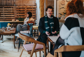 Two friends are engaged in a lively conversation inside a cozy and stylish cafe. Other patrons are seen relaxing in the background, creating a warm and welcoming environment.