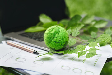 Eco-friendly business concept with green earth model, laptop, leaves, and analytics charts. Symbolizes sustainability, green innovation, and environmental responsibility in modern workspaces.