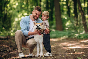 Fototapeta premium Cute pet, sitting and having fun. Father with son and dog are in the forest