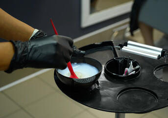 Professional hair coloring preparation in salon with gloves and red brush, mixing vibrant hair dye.  Perfect for beauty, cosmetology, hair care, salon marketing, and hairstyling visual content.