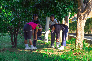 Four teen girls stretch deeply in a forward fold on a tropical park path, enjoying morning light and the surrounding greenery.
