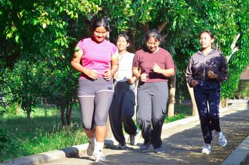 The girls laugh and jog joyfully together on a green park path surrounded by morning sunshine and tropical foliage