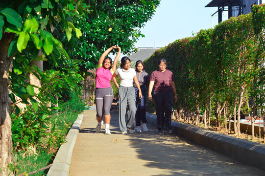 As they walk along the garden trail, one of the girls stretches her arms playfully while chatting with her friends in the leafy park. - Powered by Adobe