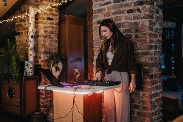 A relaxed setting where a young woman mixes music, wearing headphones and standing at a console in a warm and inviting, rustic interior.