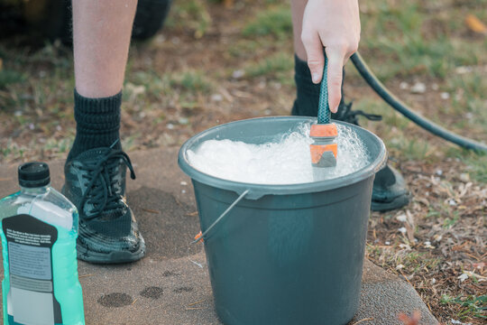 Teenage boy filling bucket with soapy water preparing to wash car