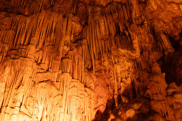 Orange lit stalactites and rock formations inside limestone cave