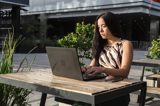 Young asian freelancer woman working on laptop outdoors in urban setting - Powered by Adobe