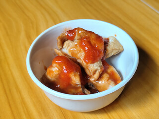 Pentol tofu served in a white bowl, pieces of tofu and meatballs covered in thick red chili sauce. Looks very delicious and delicious.