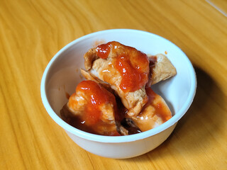 Pentol tofu served in a white bowl, pieces of tofu and meatballs covered in thick red chili sauce. Looks very delicious and delicious.