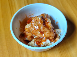 Pentol tofu served in a white bowl, pieces of tofu and meatballs covered in thick red chili sauce. Looks very delicious and delicious.