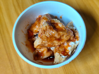 Pentol tofu served in a white bowl, pieces of tofu and meatballs covered in thick red chili sauce. Looks very delicious and delicious.