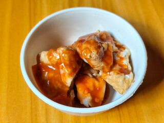 Pentol tofu served in a white bowl, pieces of tofu and meatballs covered in thick red chili sauce. Looks very delicious and delicious.