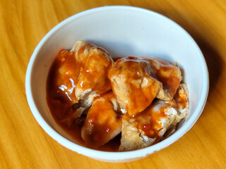 Pentol tofu served in a white bowl, pieces of tofu and meatballs covered in thick red chili sauce. Looks very delicious and delicious.