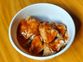 Pentol tofu served in a white bowl, pieces of tofu and meatballs covered in thick red chili sauce. Looks very delicious and delicious.
